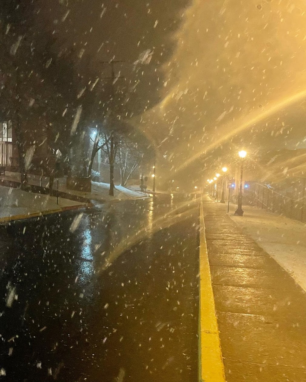 A blurry photo of a street. There is snow falling from the sky.